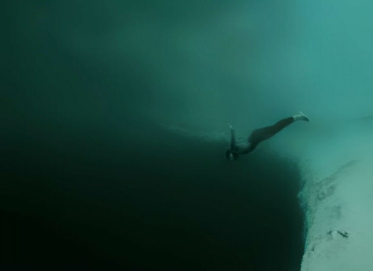 A diver swims downward into a dark, seemingly bottomless abyss in the ocean.